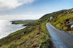La Ruta Costera de la Calzada es un testimonio del patrimonio geológico y mítico de la región. Con una extensión de 212 kilómetros desde Belfast hasta Derry, presenta un paisaje extraordinario salpicado de monumentos inolvidables. La Calzada del Gigante, declarada Patrimonio de la Humanidad por la UNESCO, cuenta con fascinantes columnas hexagonales de basalto formadas hace millones de años, que evocan antiguos fuegos volcánicos bajo la superficie terrestre. Estas esculturas naturales enmarcan las historias del legendario gigante Finn McCool, enriqueciendo el viaje con folclore y vistas impresionantes. Cerca de allí, el Puente de Cuerda de Carrick-a-Rede ofrece un emocionante cruce sobre un impresionante abismo, invitando a los viajeros a experimentar en primera persona la fuerza bruta del Atlántico. Las ruinas medievales del Castillo de Dunluce, encaramadas precariamente en el borde del acantilado, contribuyen aún más al encanto atmosférico de la ruta.